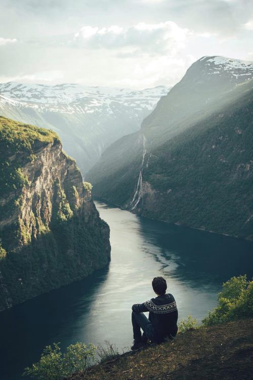 A boy sitting at the top of mountain watching nature scenes